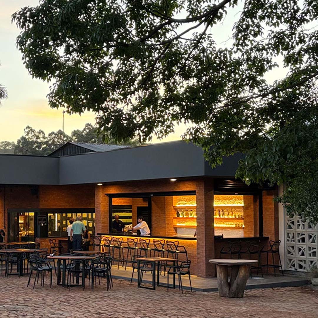 Área externa do restaurante Mama Mariinha ao entardecer, com mesas ao ar livre e bar iluminado.